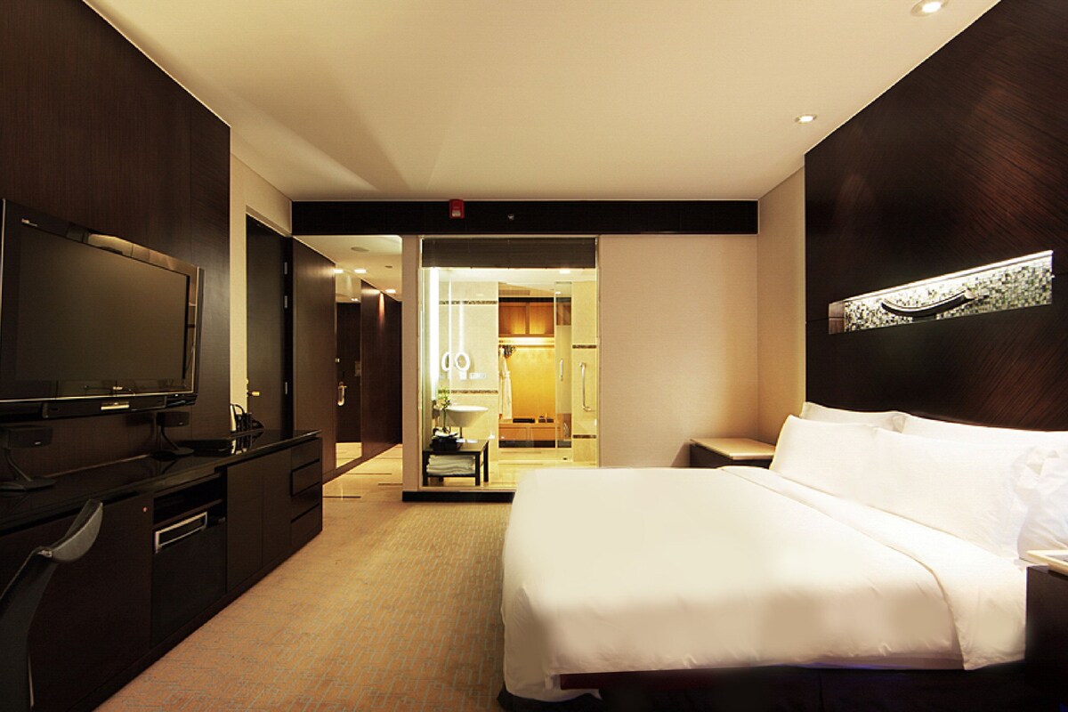 Ein Hotelzimmer mit einem großen Bett, einem Flachbildfernseher, einem Schreibtisch und einem durch eine offene Tür einsehbaren Badezimmer.