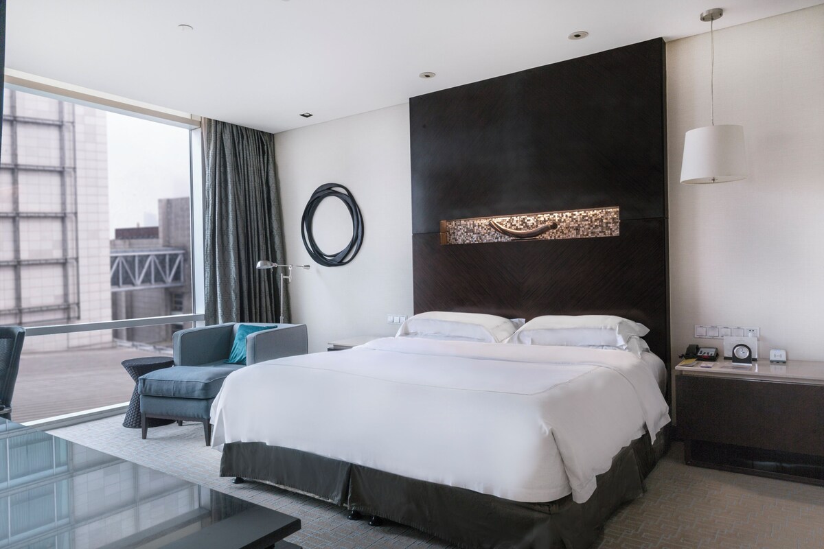 A modern hotel room with a large bed, a desk, and a view of the city.