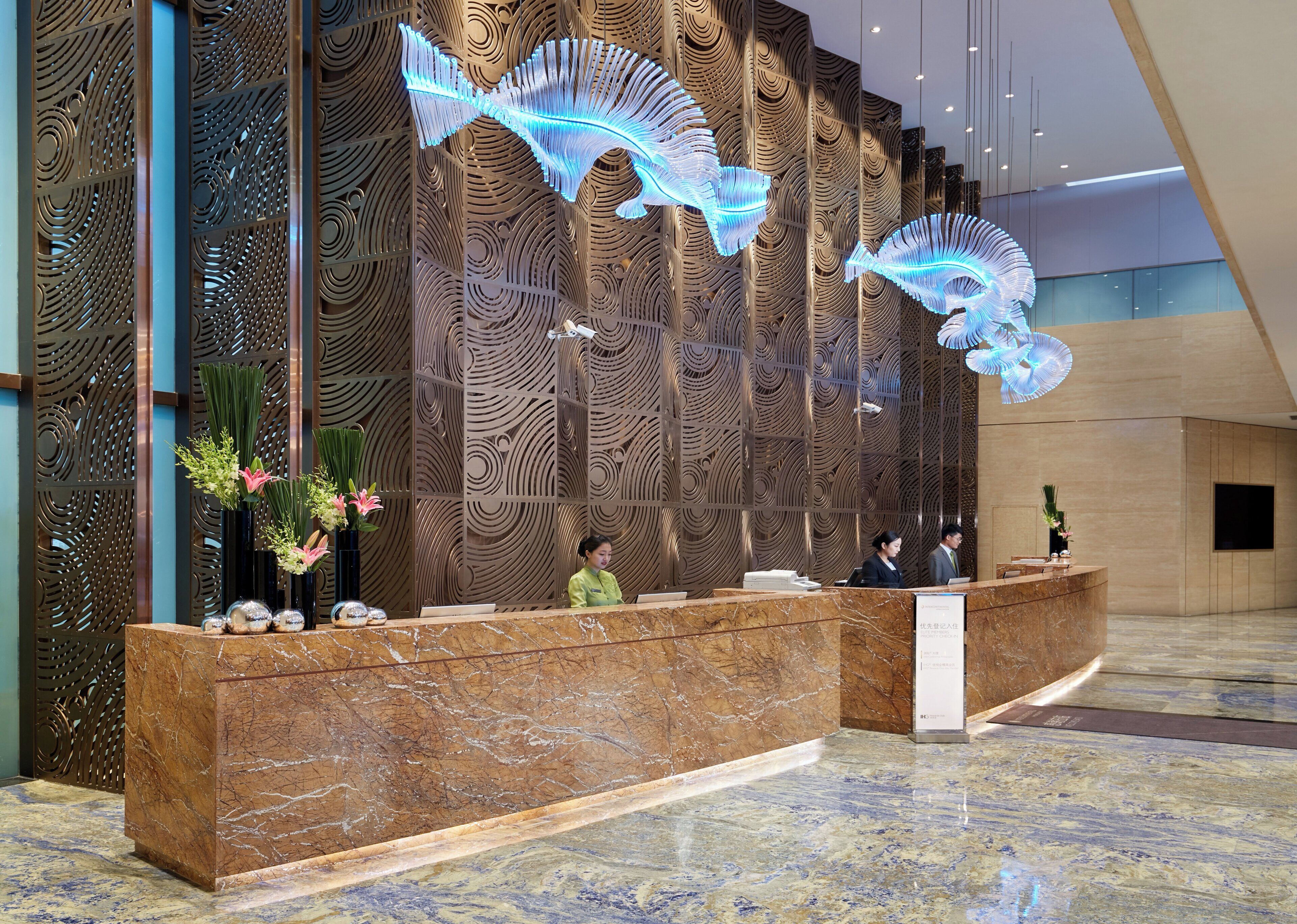 Una recepción con mostrador de mármol, una pared decorativa con diseño de olas y una escultura de pez iluminada en azul.