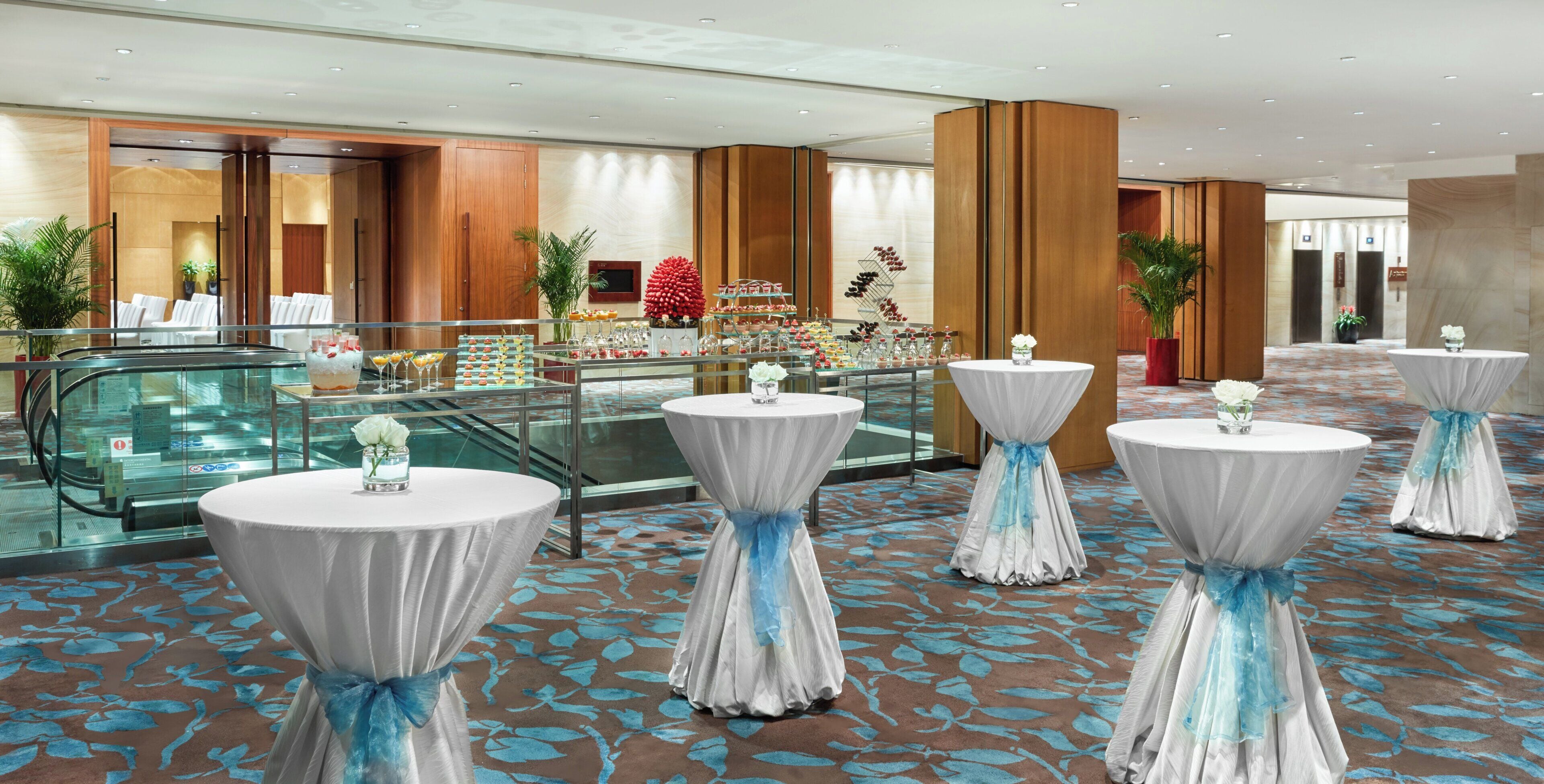 A hotel lobby with round tables, a glass elevator, and a buffet area.
