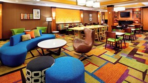 Un vestíbulo de hotel con una alfombra colorida, un sofá azul, un sillón marrón y una mesa redonda.