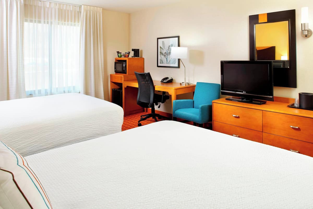 Une chambre d’hôtel avec deux lits, un bureau avec un ordinateur, une télévision, une chaise, une lampe et un four à micro-ondes.