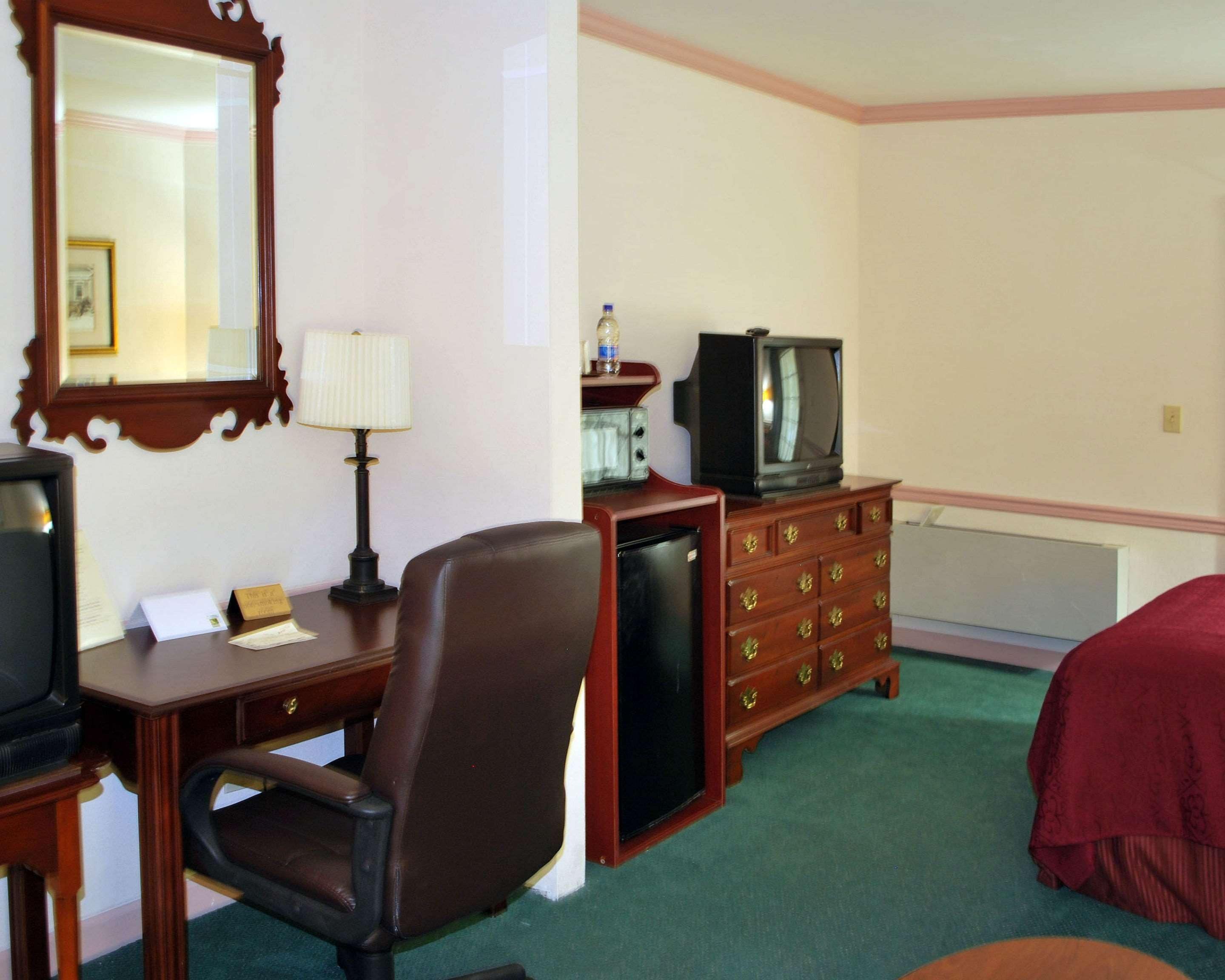 A hotel room with a desk, chair, dresser, television, and a bed.