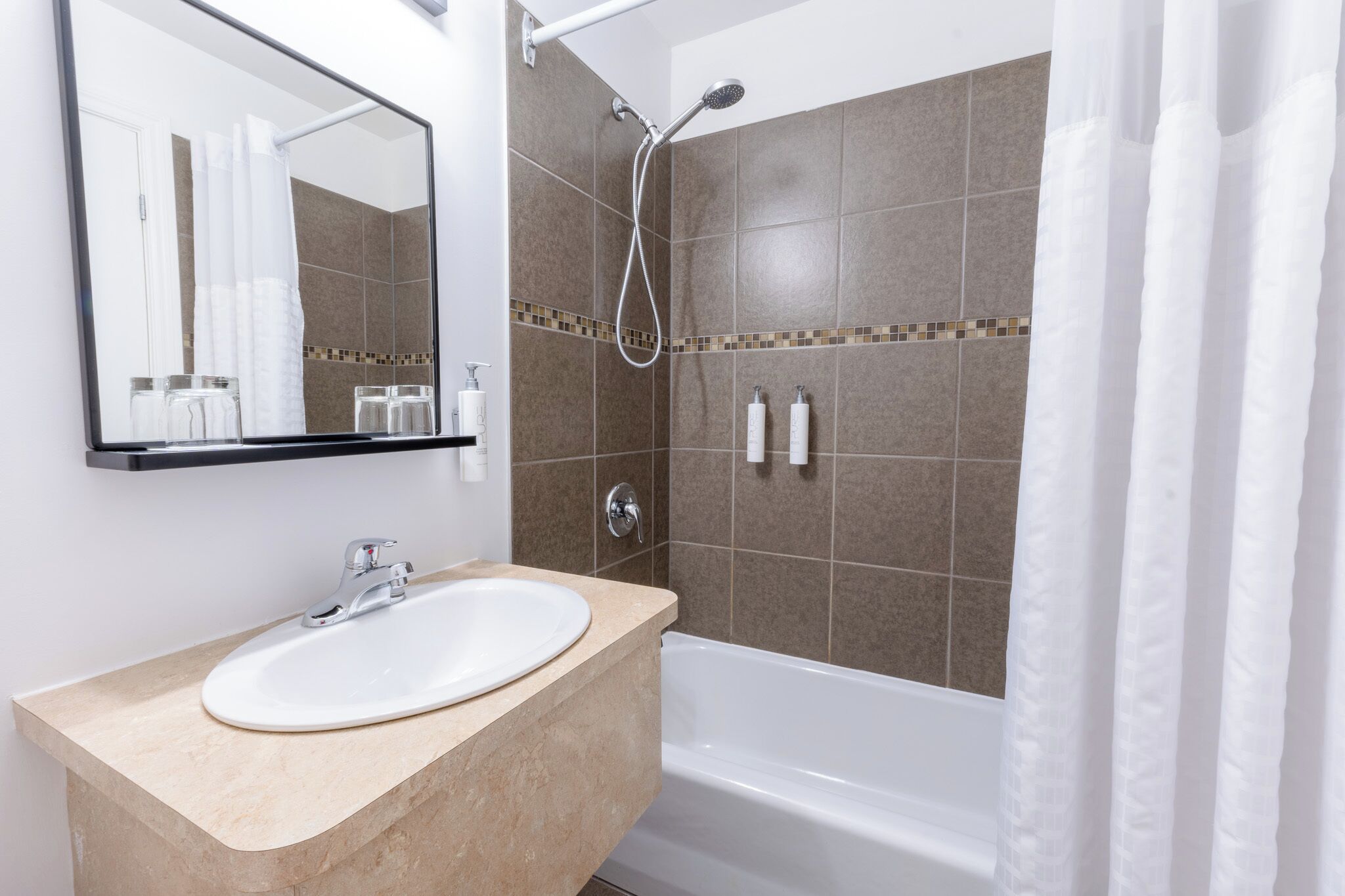 A bathroom with a sink, mirror, shower, and tiled walls.