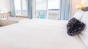 Habitación de hotel con una cama grande, una bañera, vista al mar y una silla azul junto a la ventana.