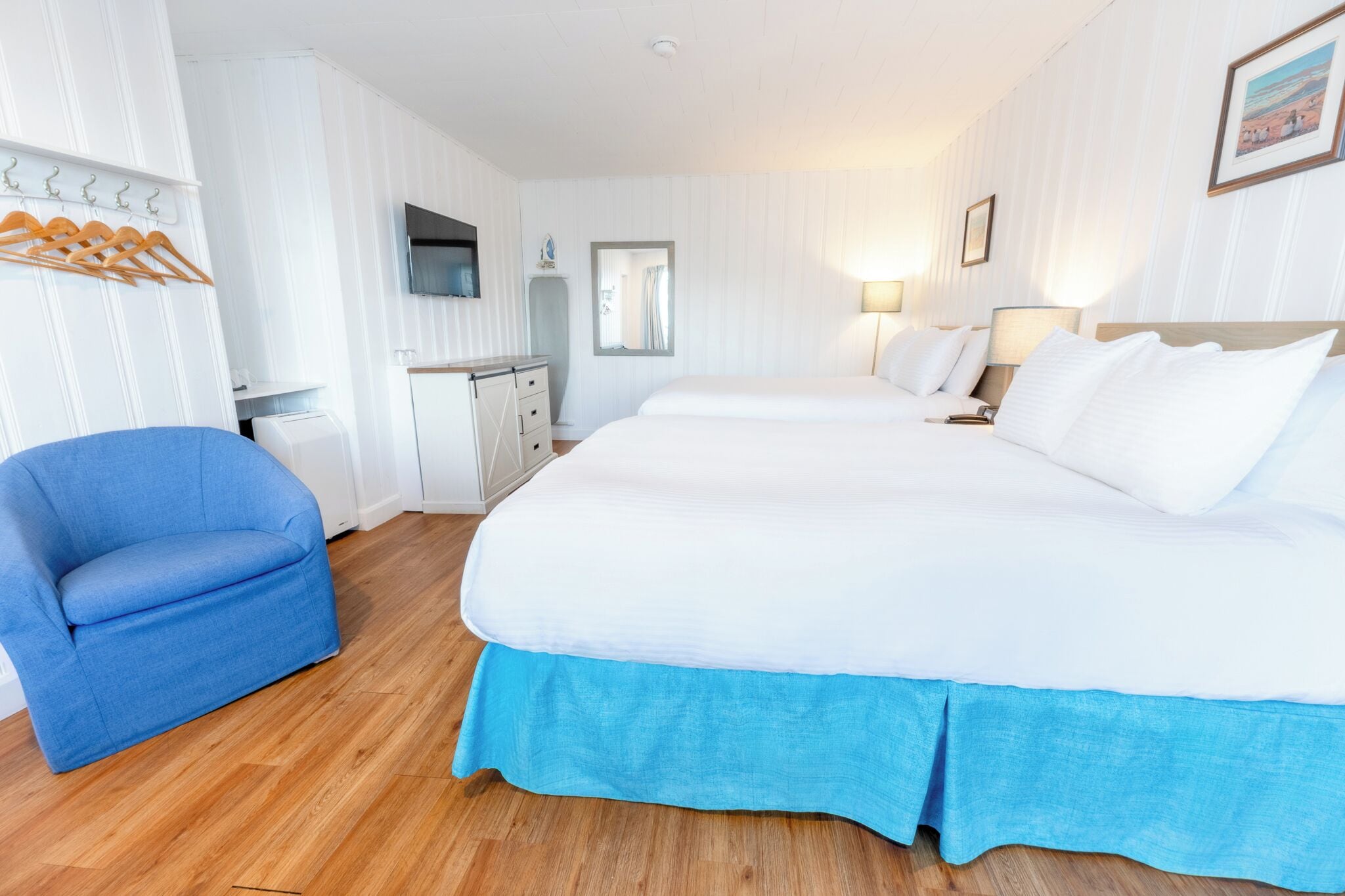 Una habitación de hotel con una cama grande, un sillón azul, un escritorio con una silla y un televisor montado en la pared.