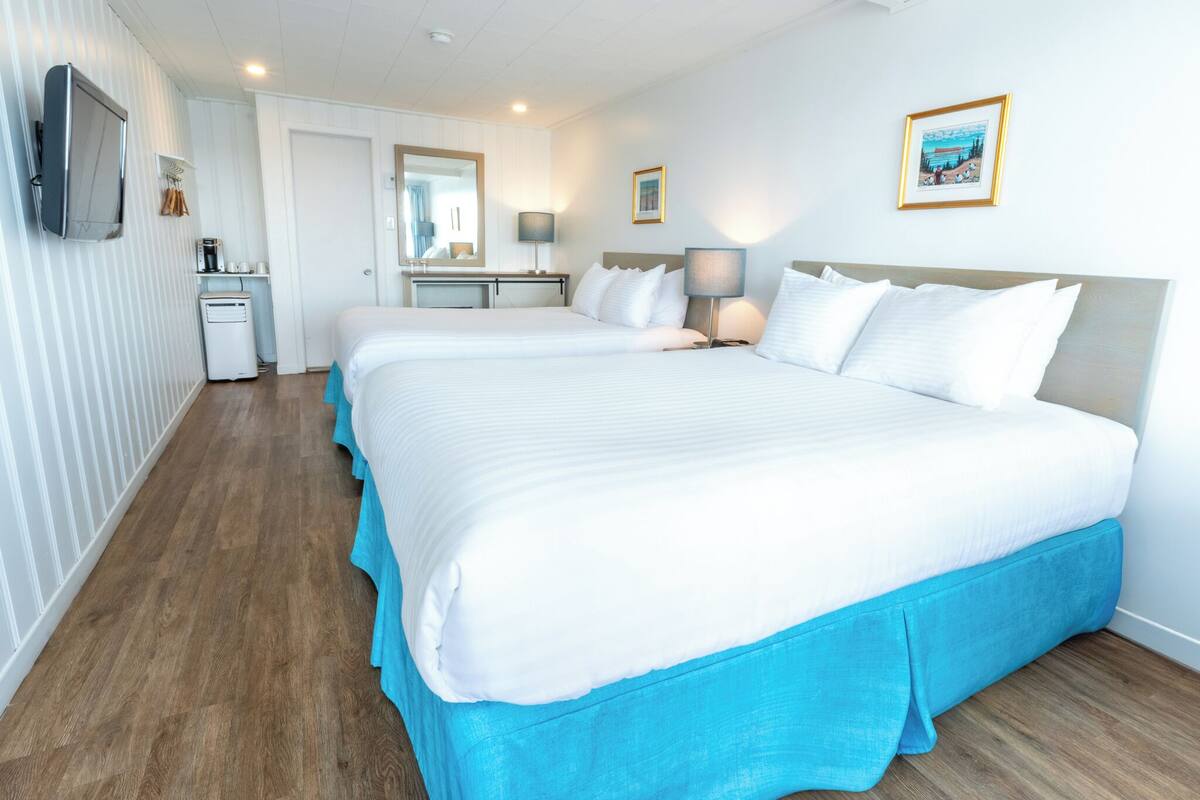 Una habitación de hotel con dos camas grandes, un escritorio, un espejo y un televisor.