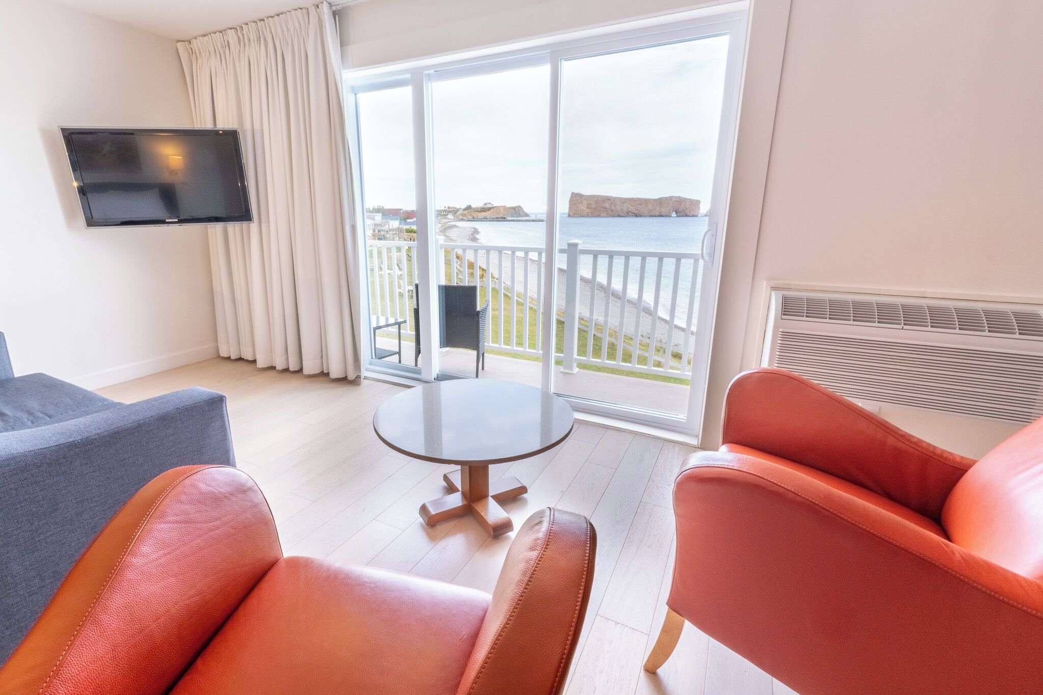 A modern room with a large balcony, a flat-screen TV, and leather chairs.