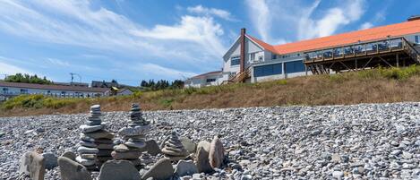 Una propiedad costera con playa de guijarros, terraza de madera y casa con techo rojo.