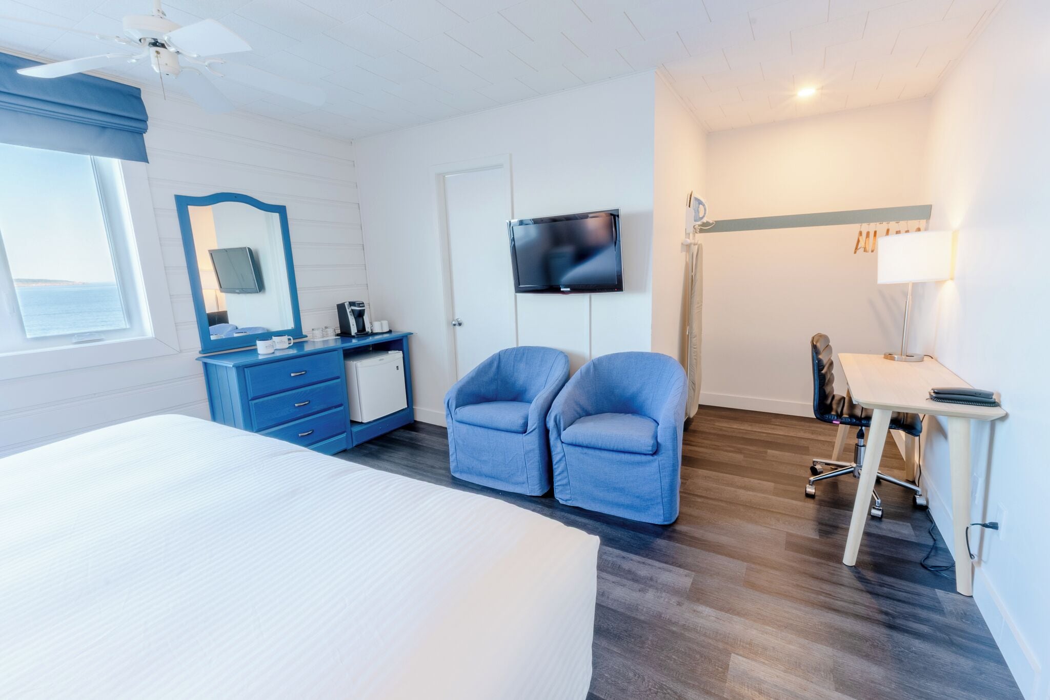 Quarto de hotel com cama, escrivaninha com cadeira, televisão, guarda-roupa e janela com vista.