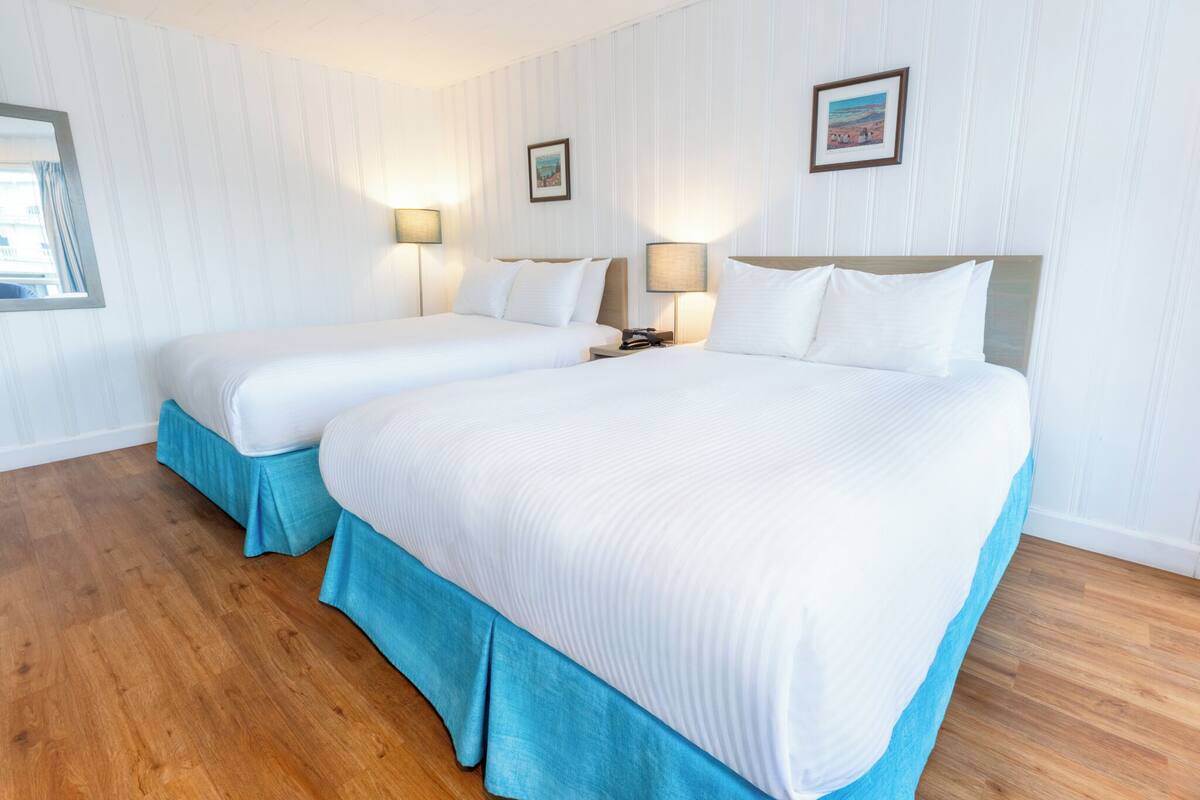 Habitación de hotel con dos camas, suelo de madera y una ventana con cortinas.