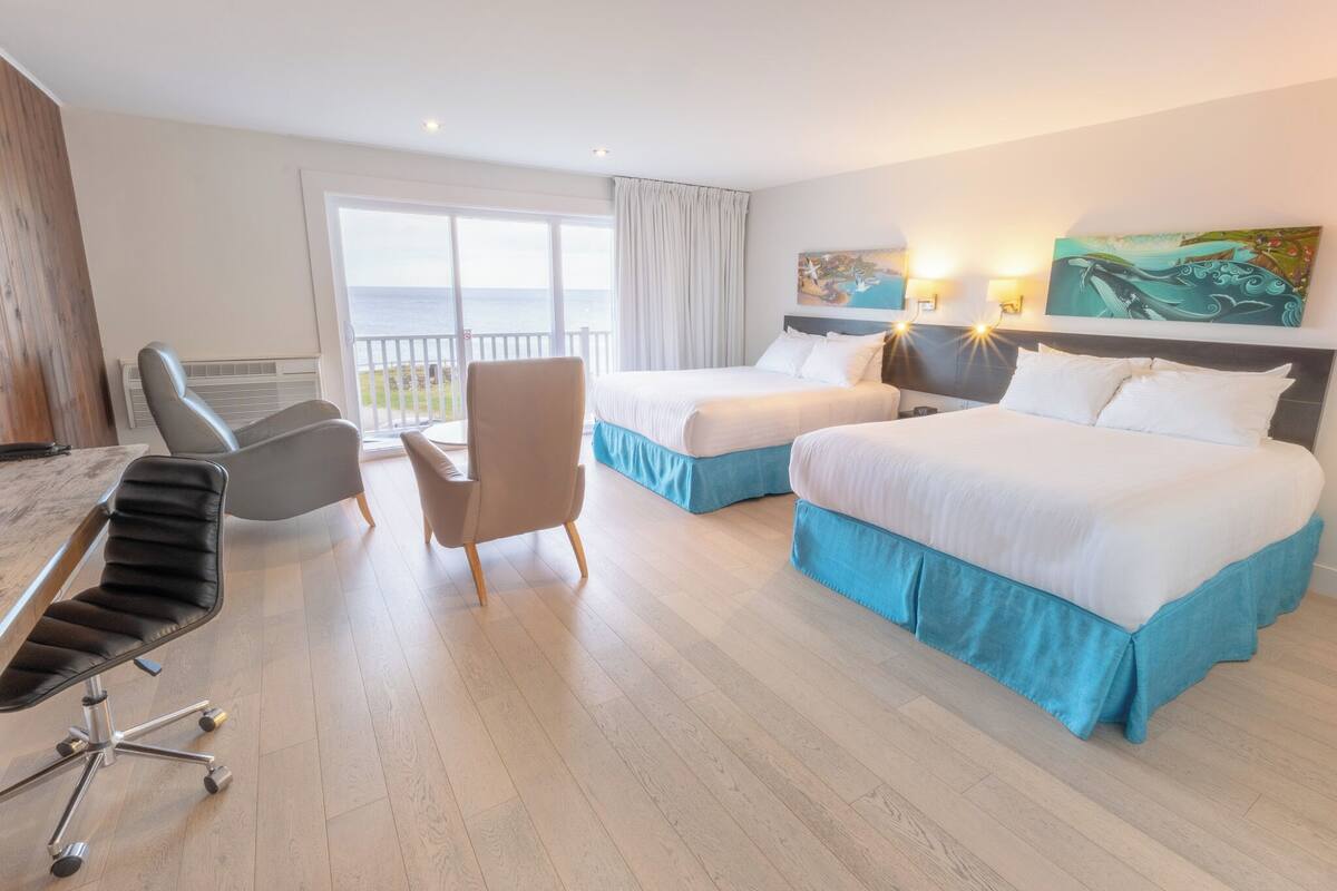 Habitación de hotel con dos camas, un escritorio, una silla y vistas al mar.