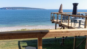 Terraza de madera con asientos al aire libre, con vista a una playa y al mar.