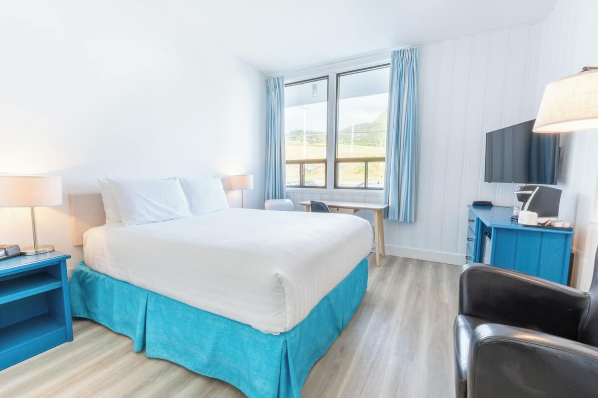 Habitación de hotel con cama, escritorio, silla, televisor y ventana con cortinas.