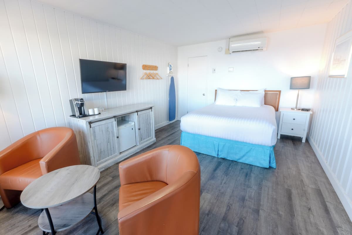Una habitación de hotel con una cama, dos sillones naranjas, una mesita, un televisor, un aparador y una mesita de noche con una lámpara.