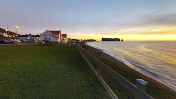 A coastal area with a grassy promenade, a wooden fence, and a building with a red roof.