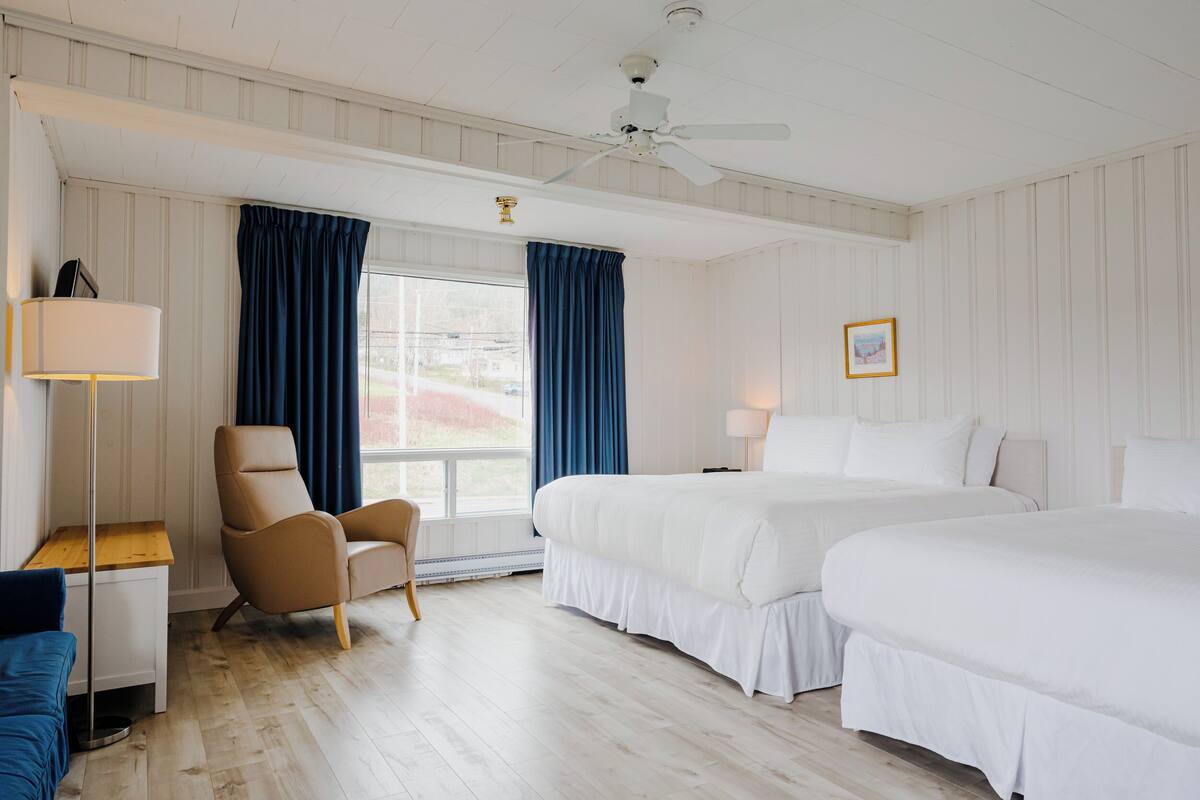 Habitación de hotel con dos camas, un escritorio, una silla, una lámpara de pie y un ventilador de techo.