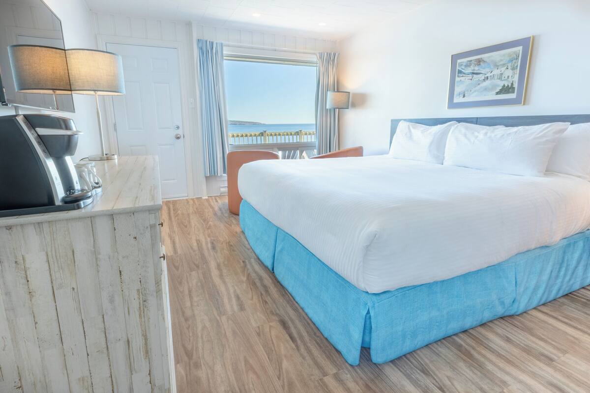 Habitación de hotel con cama, escritorio con lámpara, una silla y vista al mar.