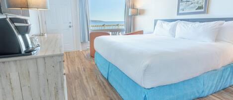 Een hotelkamer met een bed, een bureau met een lamp, een stoel en uitzicht op zee.
