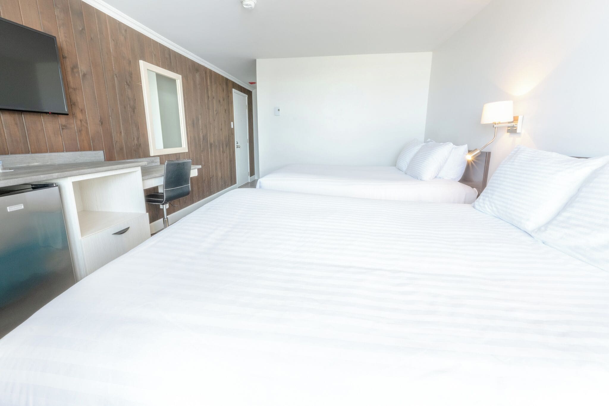 Habitación de hotel con dos camas, un escritorio, un televisor y una lámpara de pared.