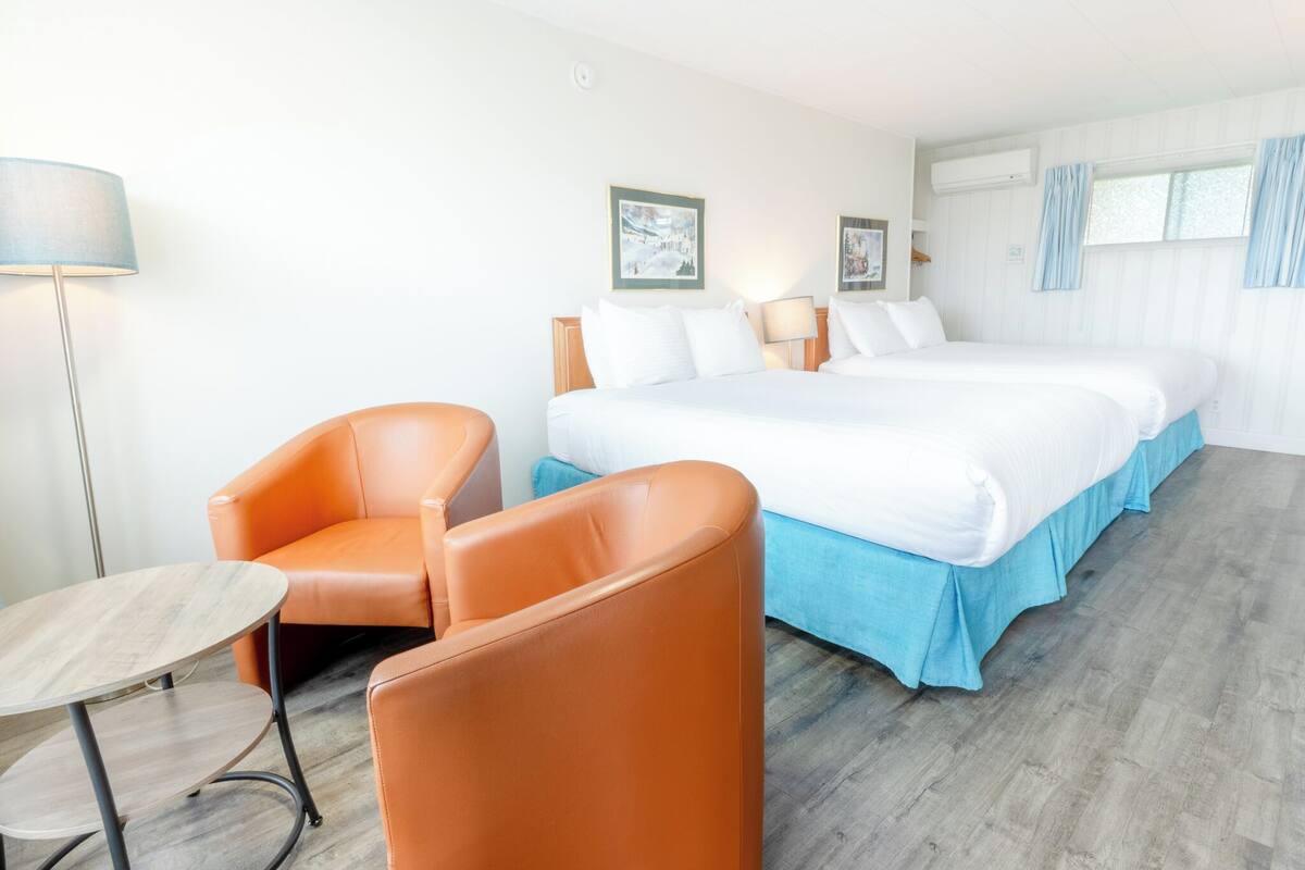Una habitación de hotel con una cama doble, dos sillas naranjas, una mesita y una lámpara.
