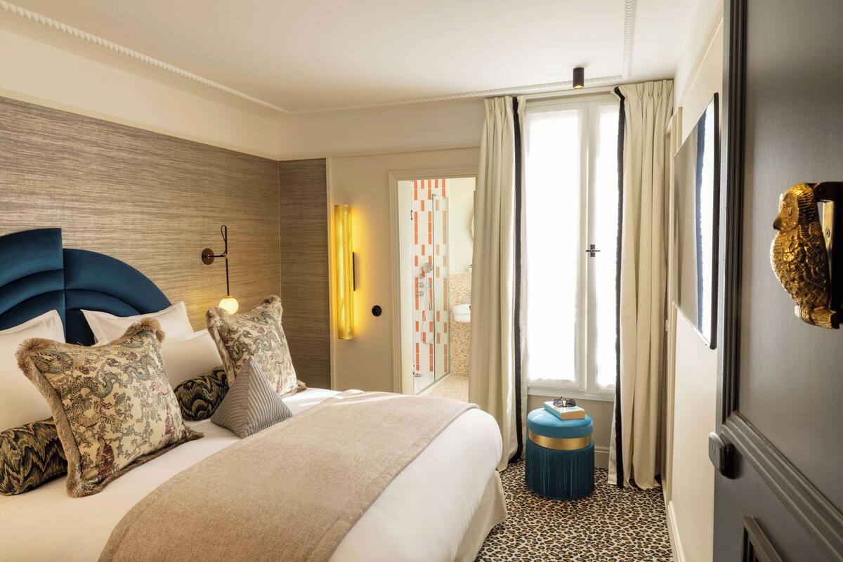 A hotel room with a large bed, a headboard, a bedside table, and a door leading to the bathroom.