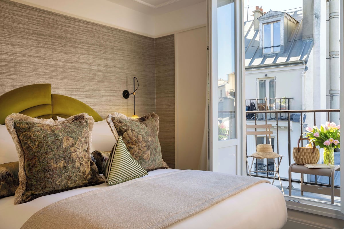 A bedroom with a large bed, a headboard, and a view of a balcony with a wicker chair and a basket.
