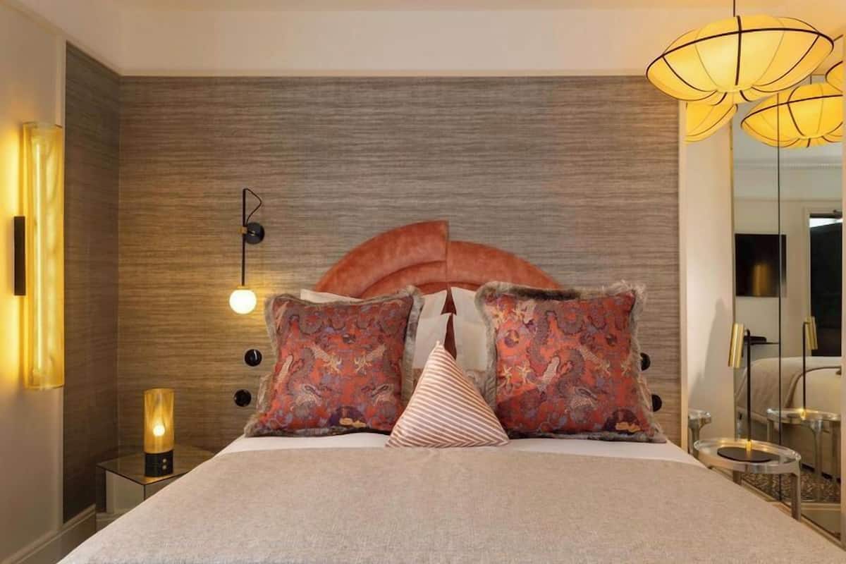 A modern bedroom with a large bed, decorative pillows, a wall-mounted light, and a bedside table with a lamp.