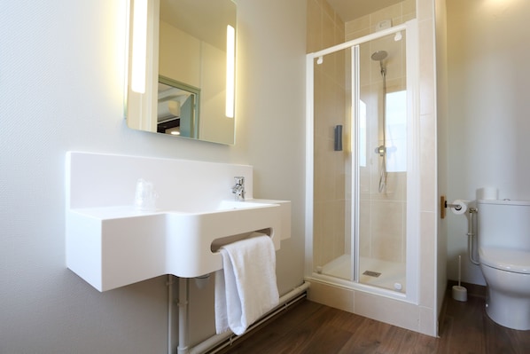 Un baño moderno con lavamanos blanco, espejo y cabina de ducha con paredes de vidrio.