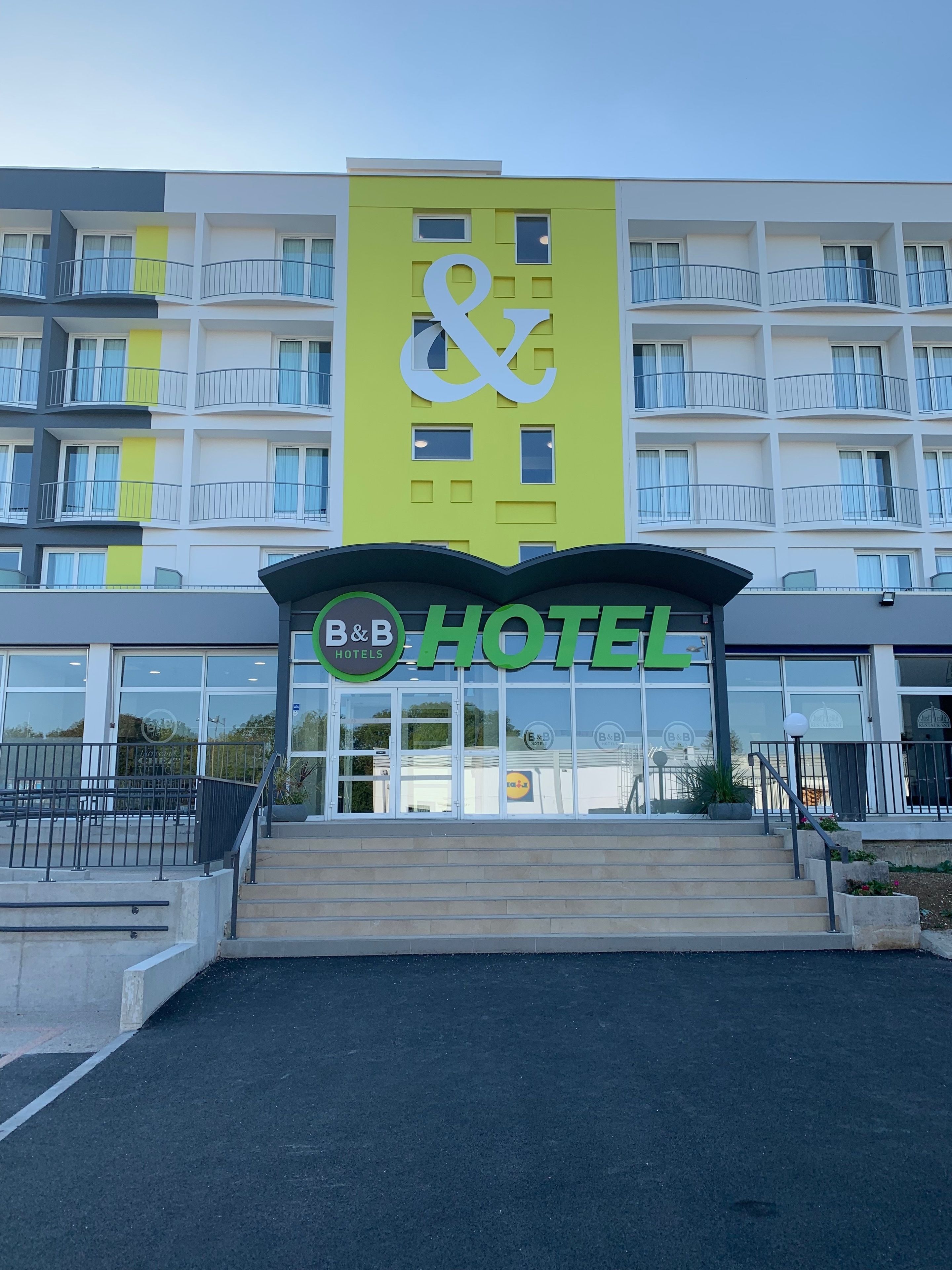 A B&B hotel with a modern design, featuring a prominent sign and a staircase leading to the entrance.