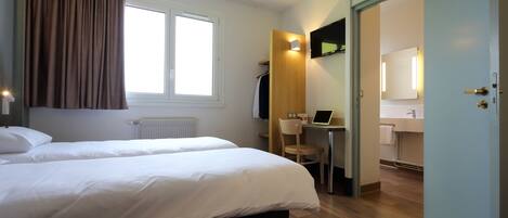 A hotel room with two beds, a desk with a chair, a mirror, and a bathroom visible through an open door.