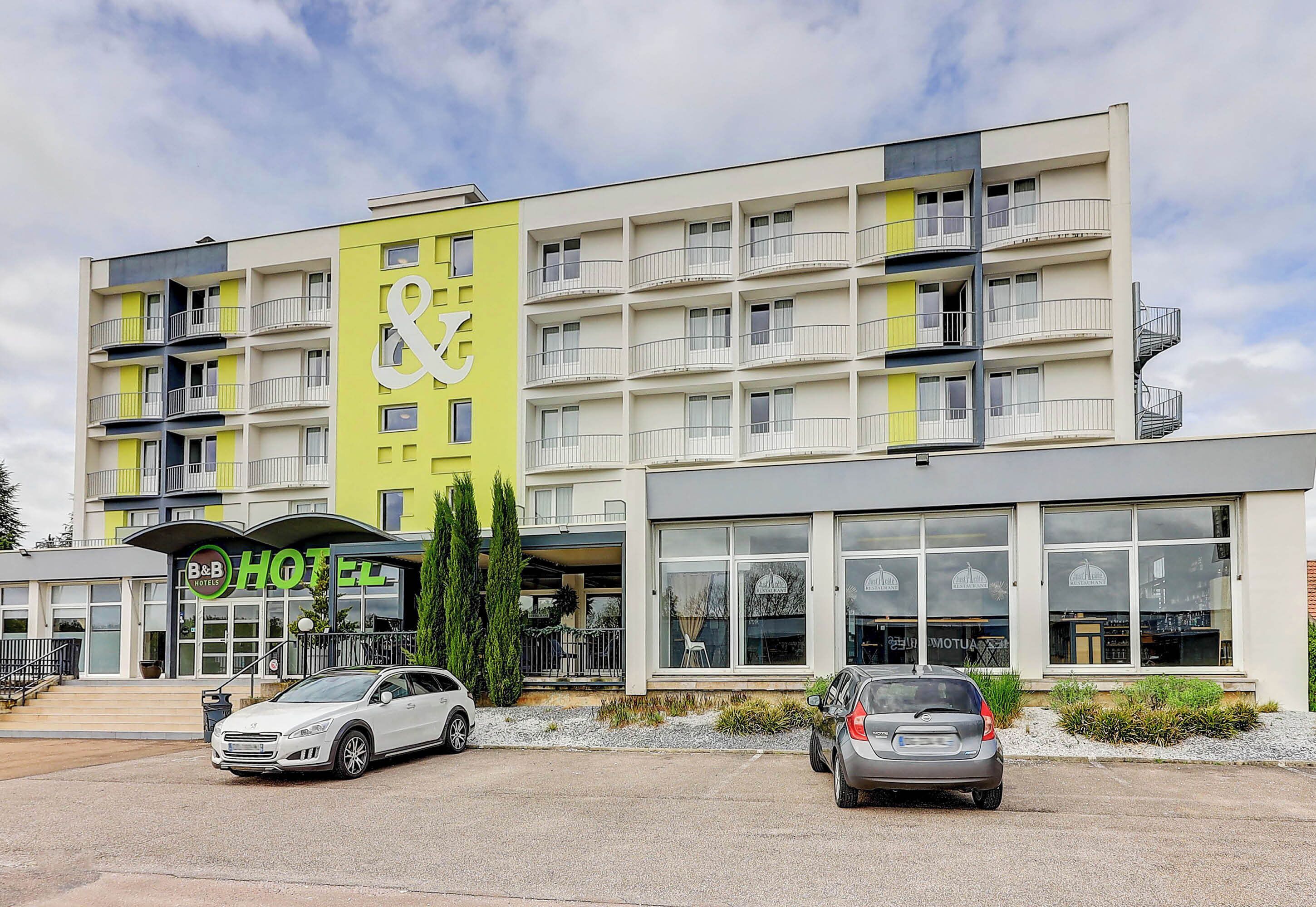 Ein Hotel mit gelb-weißer Fassade, mehreren Balkonen und einem parkenden Auto vor der Tür.