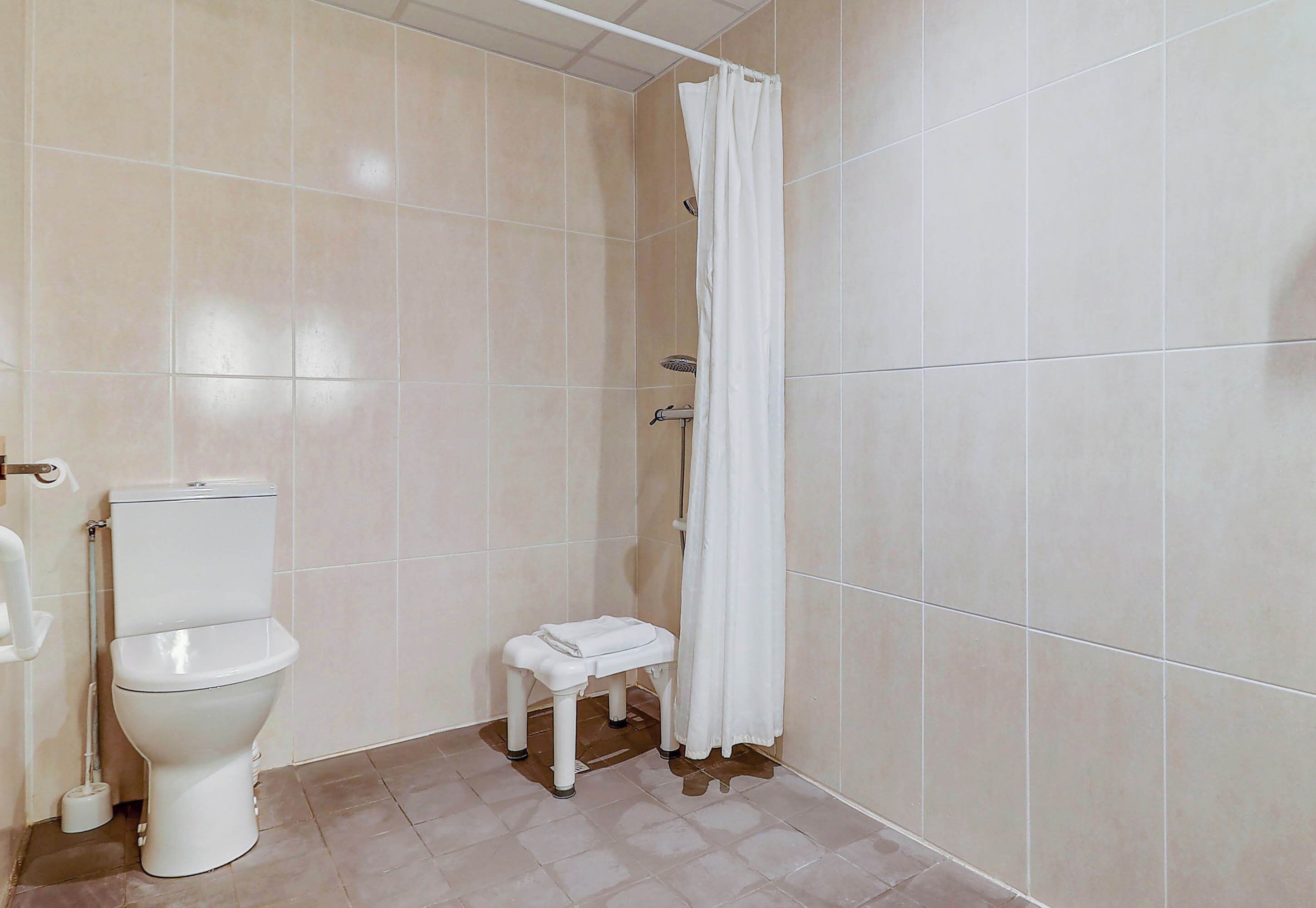 A bathroom with a toilet, a shower curtain, and a small stool.