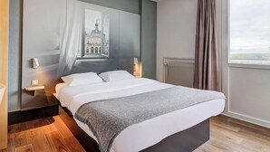 Un dormitorio moderno con una cama grande, una mesita de noche, una lámpara de pared y una ventana con cortinas.