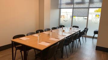 Un salón de conferencias con una mesa larga, sillas y una ventana con paneles de vidrio esmerilado.