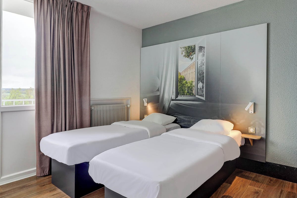 A hotel room with two beds, a large window with a view, and a modern design.