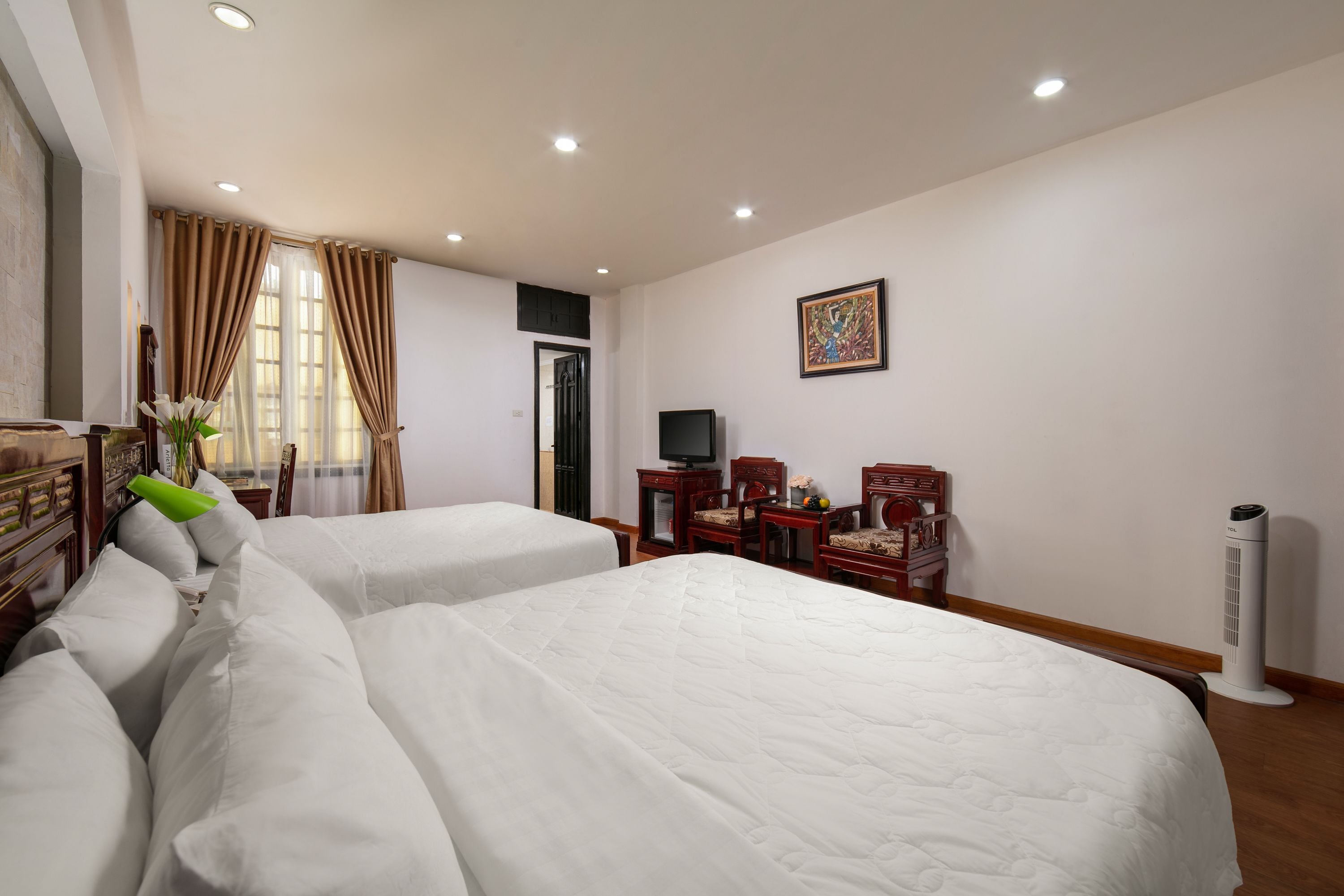 A hotel room with two beds, a desk with a chair, a television, and a standing heater.