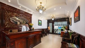 A reception area with a wooden reception desk, a chandelier, and a seating area with wooden chairs. - Little Diamond Hotel (Hanoi)