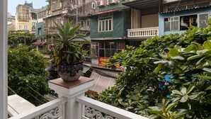 A balcony with a potted plant, a white railing, and a view of multi-story buildings. - Little Diamond Hotel (Hanoi)