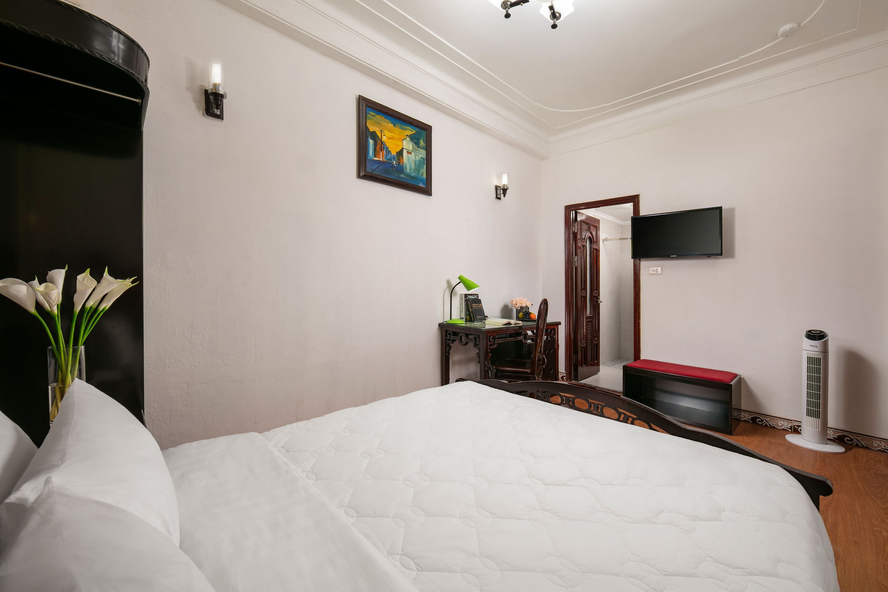 A hotel room with a large bed, a desk with a chair, a flat-screen TV, a standing heater, and a painting on the wall.
