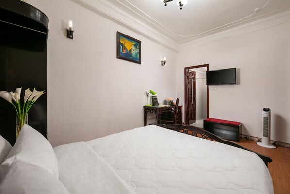 Une chambre d’hôtel avec un grand lit, un bureau avec une chaise, un téléviseur à écran plat, un radiateur et un tableau au mur.
