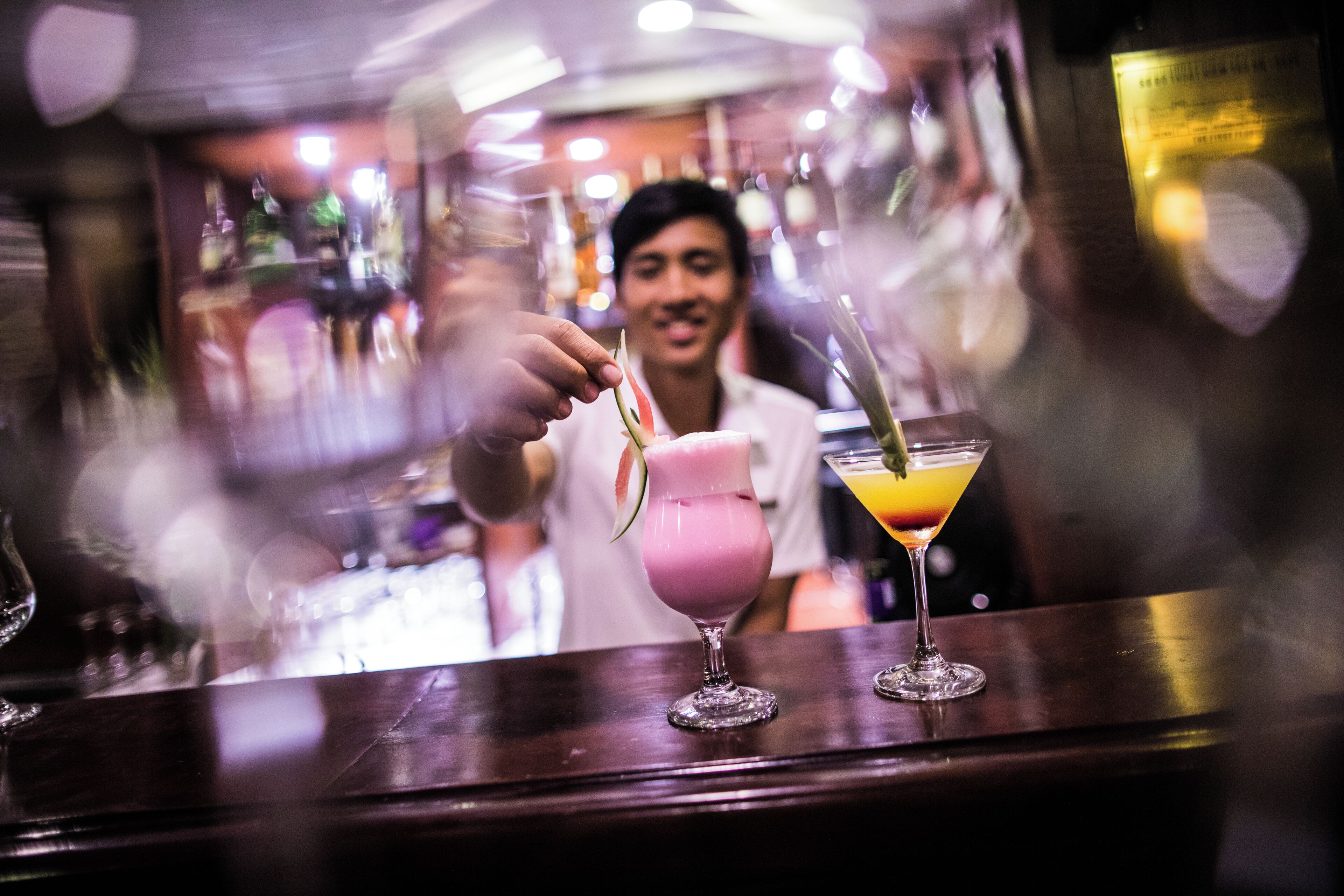 A bar with a person pouring a drink into a glass. There are two other glasses on the bar.