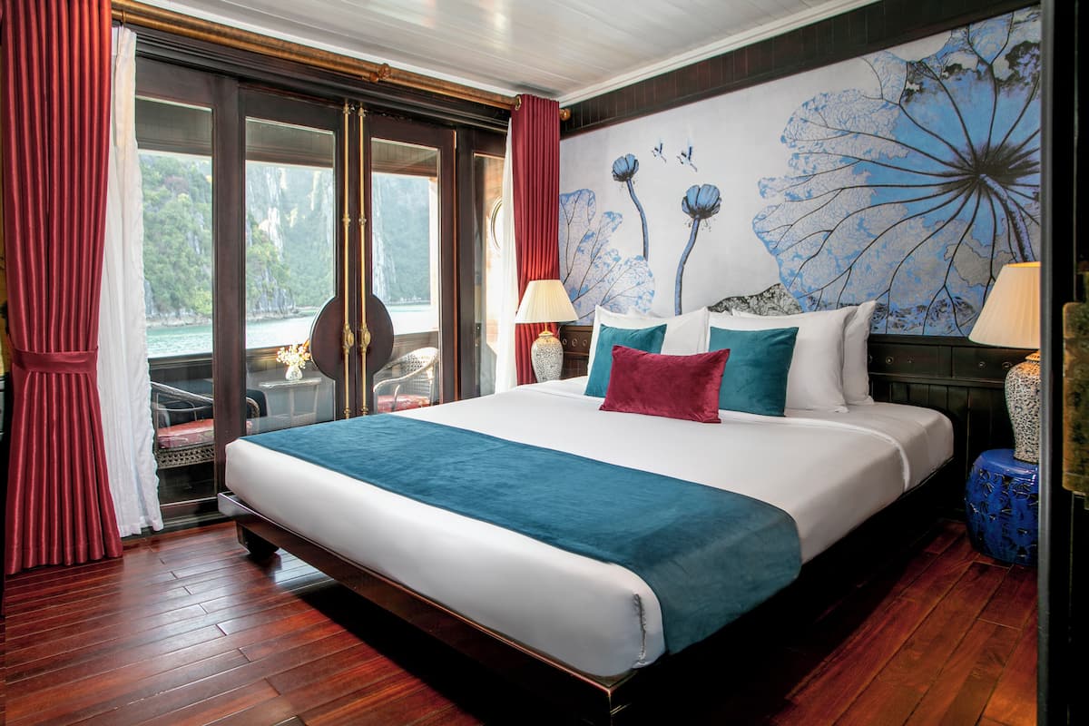 A large bed with a blue and white bedspread, red and teal pillows, and two lamps on either side.