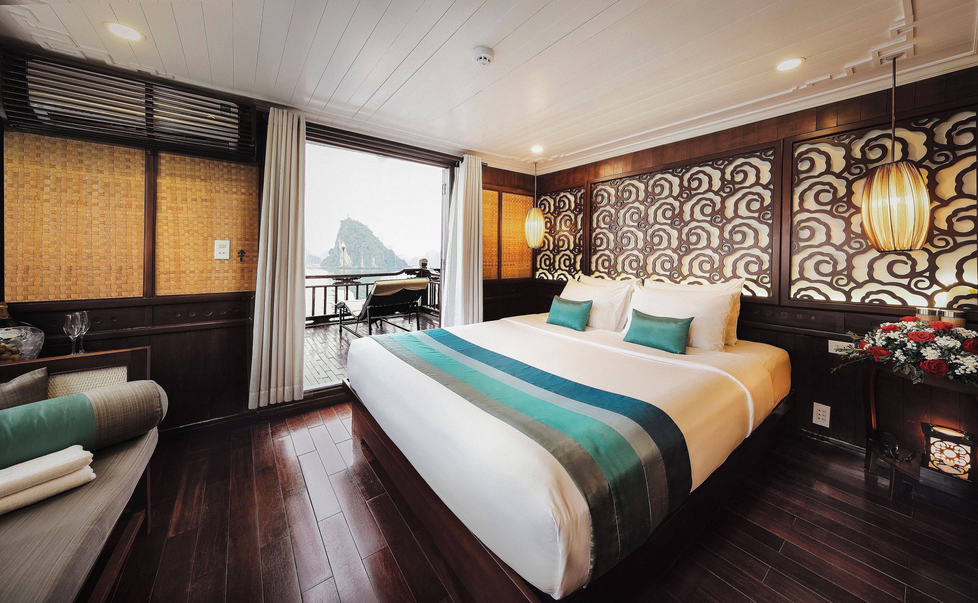 A hotel room with a large bed, a view of a mountain, a balcony with a table and chairs, and a decorative wall panel.