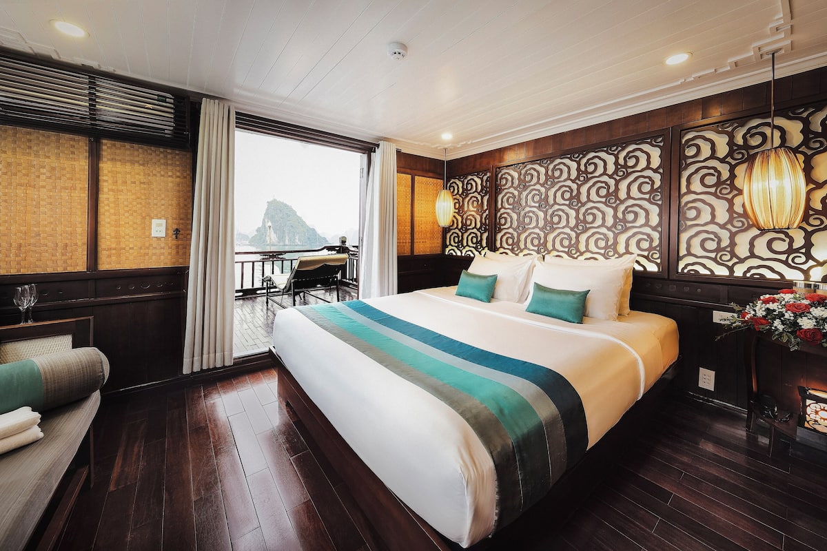 A hotel room with a large bed, a view of a mountain, a balcony with a table and chairs, and a decorative wall panel.