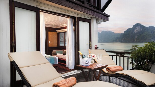 A balcony with two lounge chairs, a table with a bottle of champagne, and a view of a mountainous landscape.