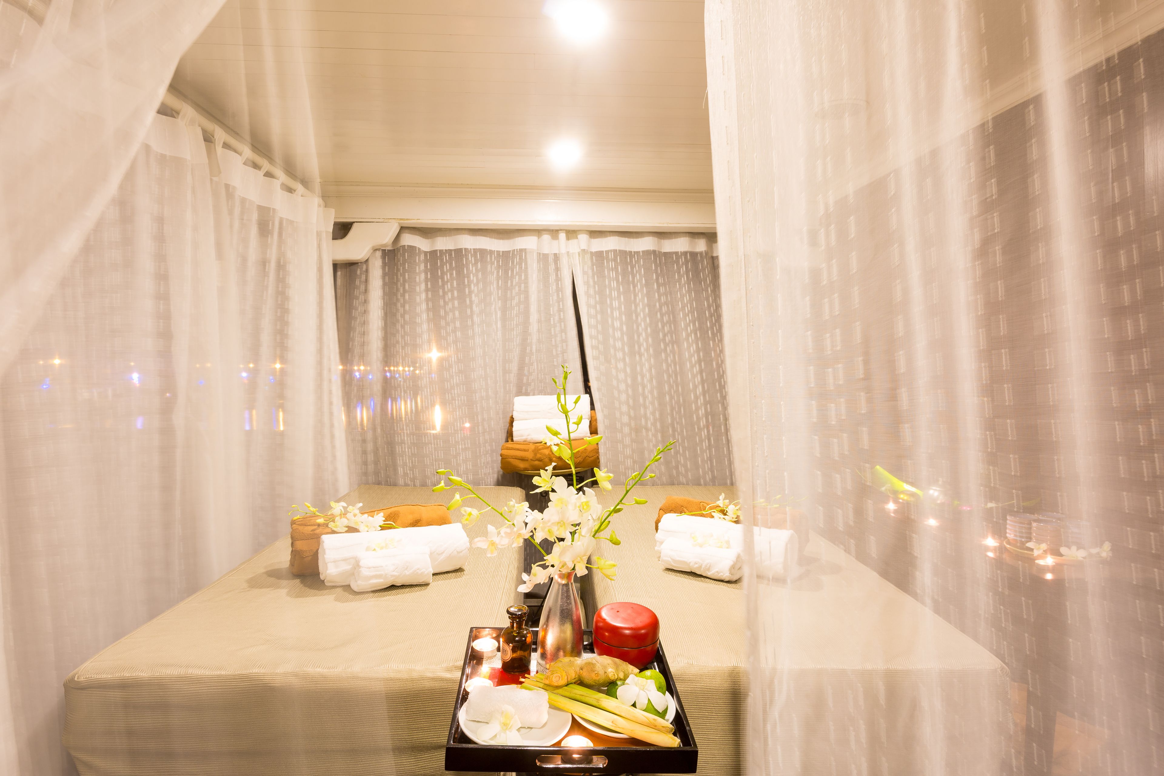 A spa treatment room with a massage table, towels, a tray with candles, flowers, and a diffuser.