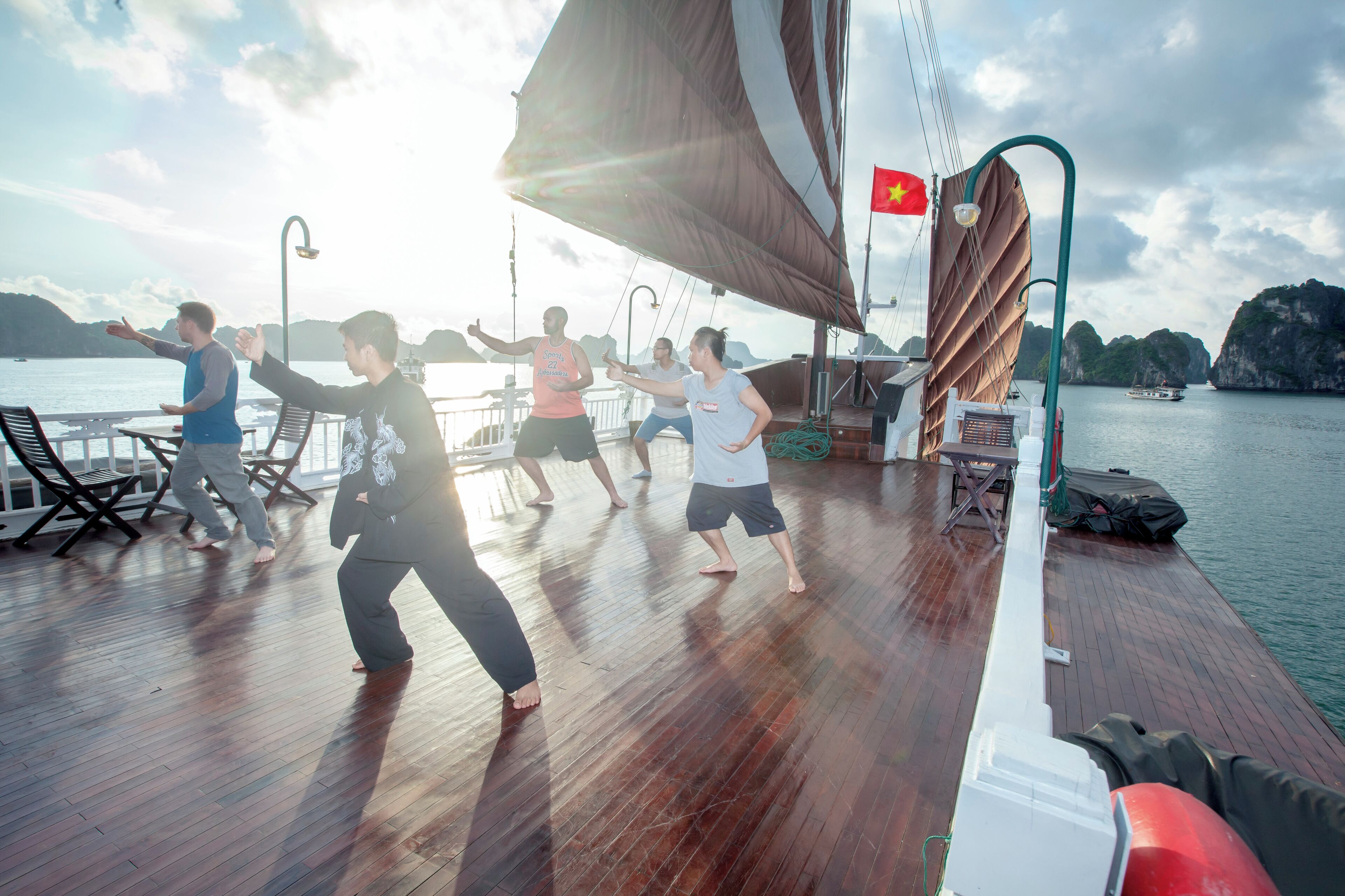 A group of people exercising on a boat deck with a flag, a railing, and a view of the water.
