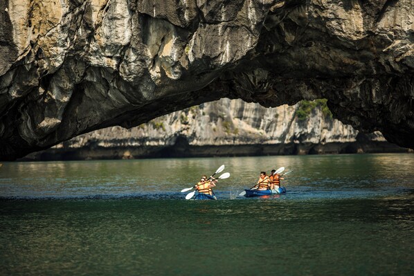 Kayakistas remando bajo un gran arco rocoso.