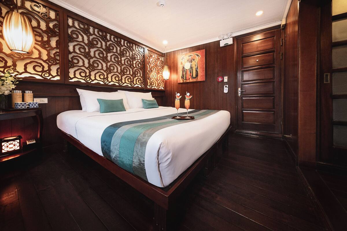 A well-appointed hotel room with a large bed, decorative wall paneling, a painting, and a wooden wardrobe.